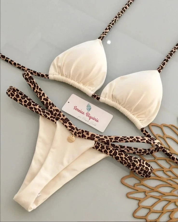 A cream colored bikini set with leopard print straps lying on a white surface next to a brand tag and decorative mat.
