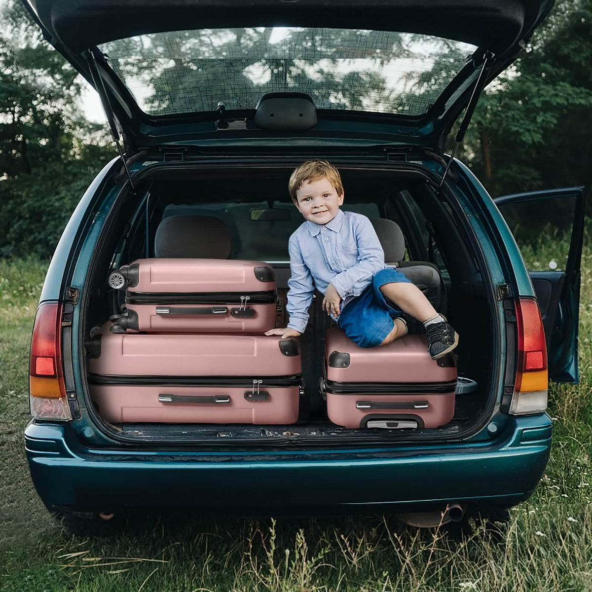 Three rose gold suitcases are packed into the open trunk of a dark green car, with a young boy sitting on top of the luggage.