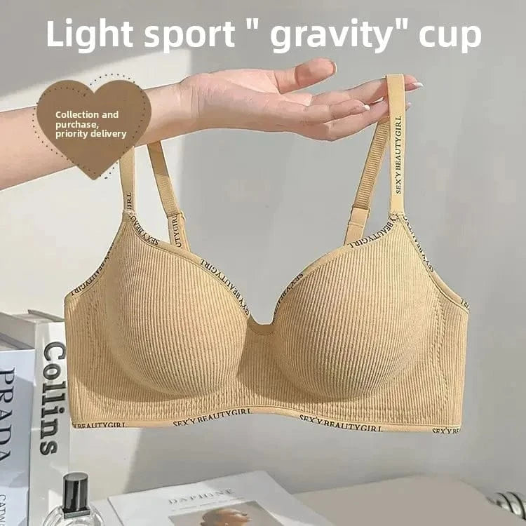 A beige ribbed wireless bra with text-patterned straps and under-band being held up in front of a white background with books.