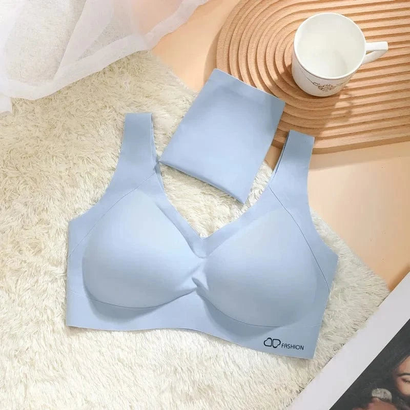 A light blue seamless bralette with a V-neckline lies on a white faux fur rug next to a matching folded garment, a white mug, and a wooden coaster.