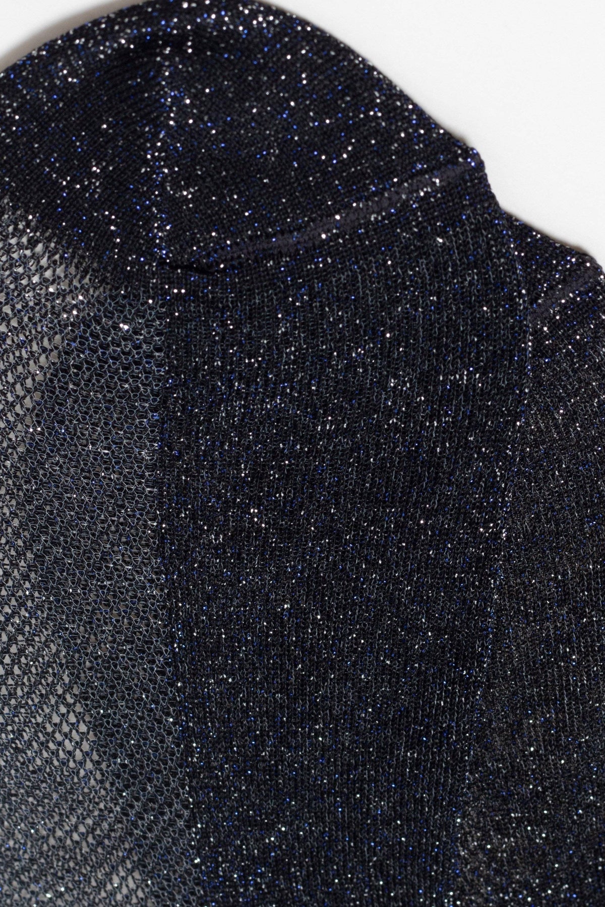 A close-up of a dark navy blue knit top featuring a shimmery, metallic finish and a subtle semi-sheer mesh texture along the left side.