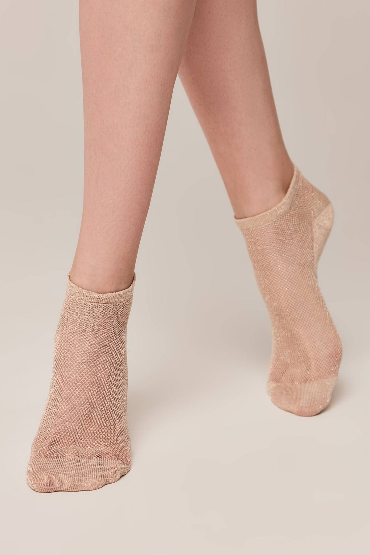 Ankle socks in a beige, fine-knit mesh texture worn on a person's feet against a plain, light background.