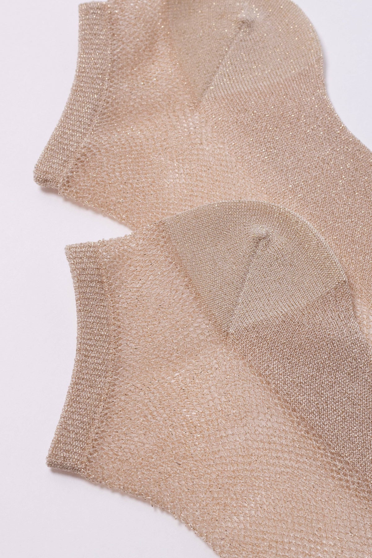 A pair of shimmering beige ankle socks with a sheer, lightweight knit texture against a white background.