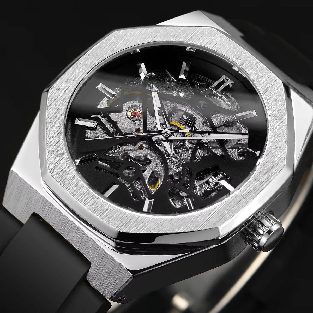 A skeleton watch with a silver-toned octagonal case, visible internal mechanical movement, and a black silicone strap set against a dark background.