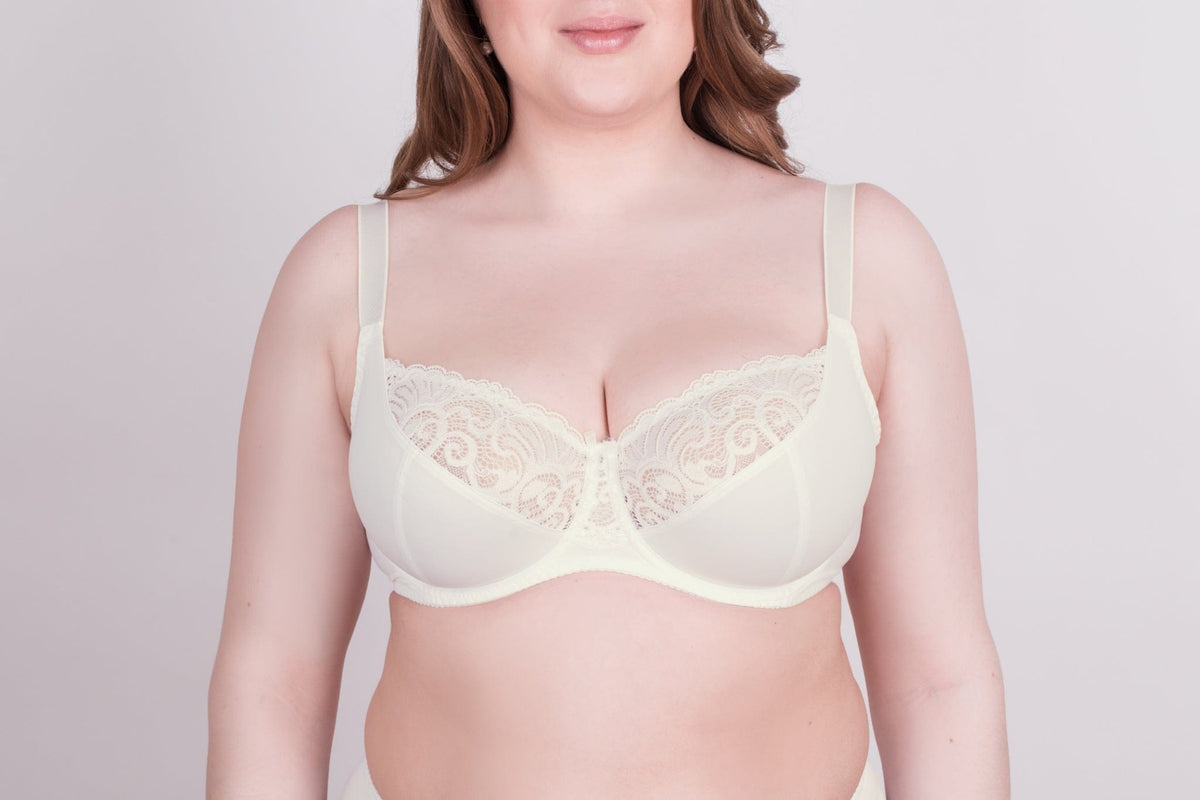 A cream-colored underwire bra featuring lace detailing on the upper cups worn by a person against a plain white background.