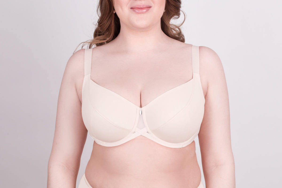 A beige full-coverage underwire bra with wide shoulder straps and a small decorative detail at the center gore worn by a person.