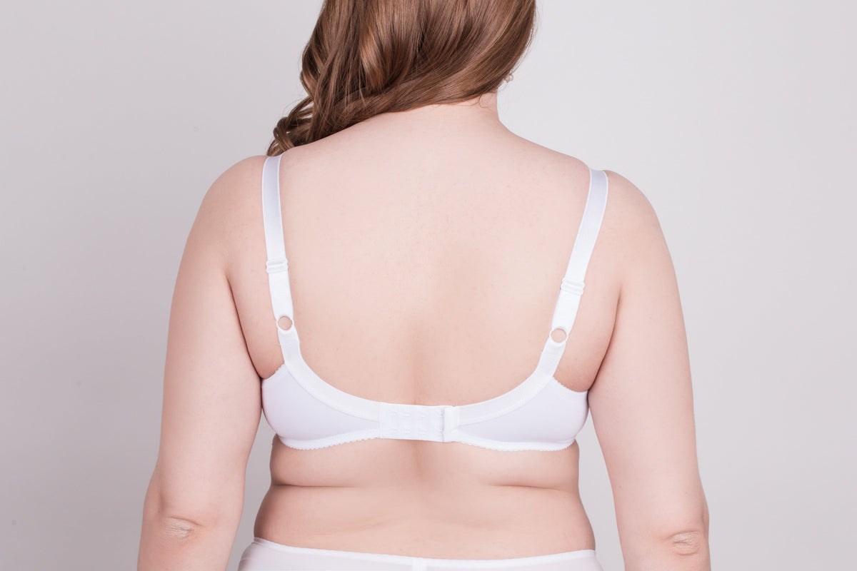 A woman seen from the back wears a white bra with thin adjustable straps against a plain light gray background.