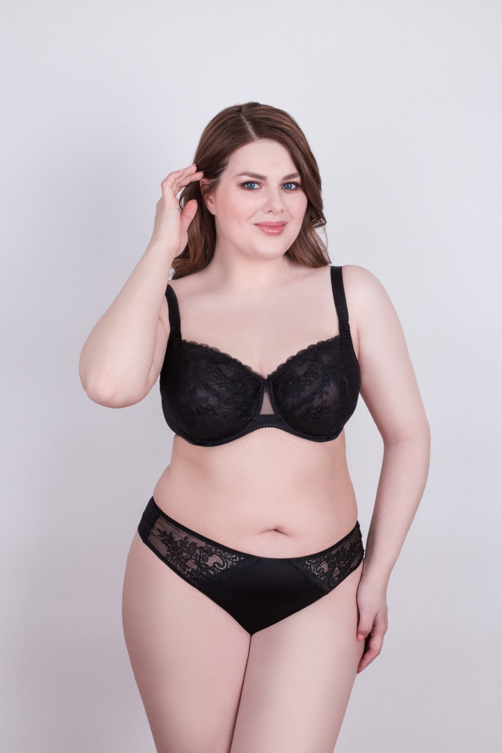 A woman wears a black lace bra and matching high-cut bikini bottoms against a light grey background.