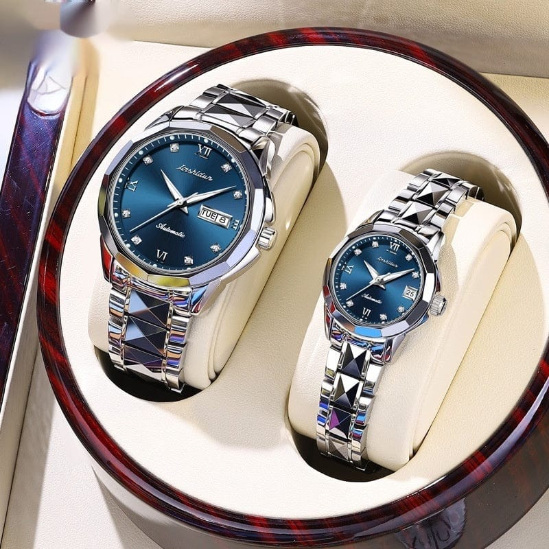 A pair of metallic watches with blue circular faces and decorative link bands sit inside an open round wooden display case.