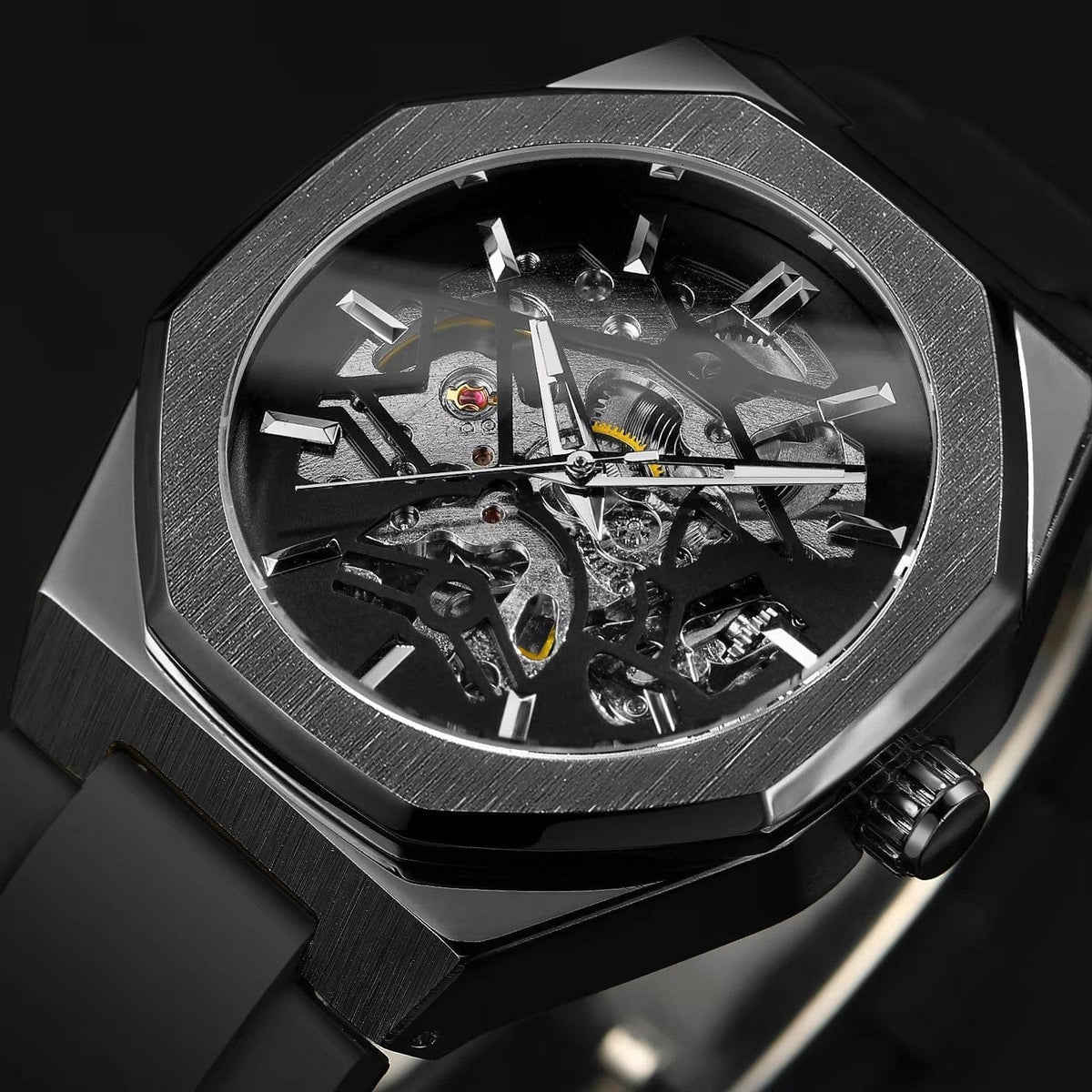 A skeleton watch with an octagonal dark metal bezel, metallic hour markers, and a black rubber strap against a dark background.