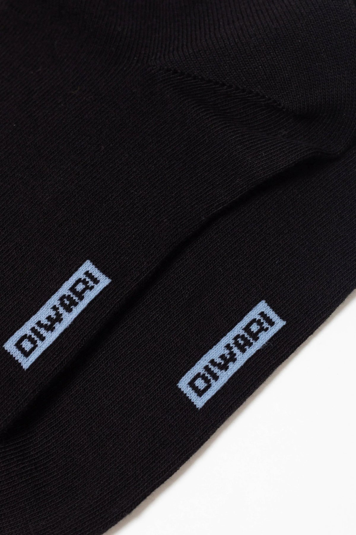 A pair of black socks features a light blue rectangular logo with the word DIWARI embroidered on the side.