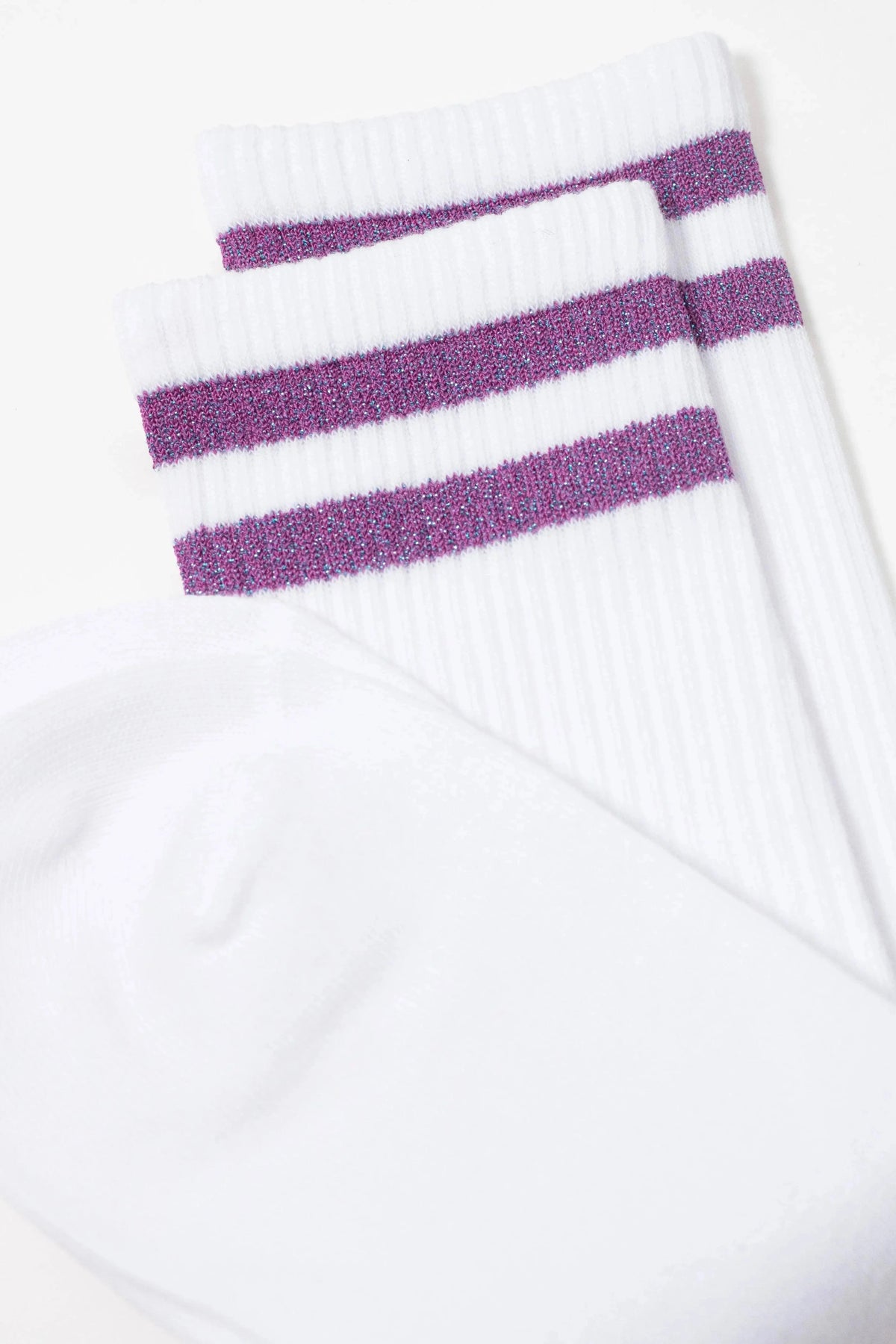A pair of white crew socks featuring two horizontal glittery purple stripes around the ribbed upper cuffs.
