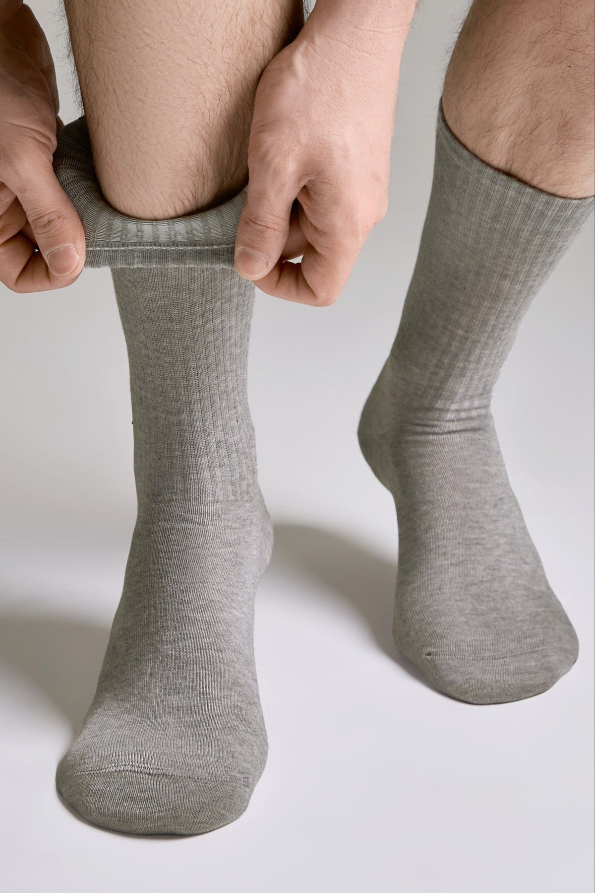 A pair of mid-calf ribbed grey socks being pulled onto a person's legs against a plain light background.