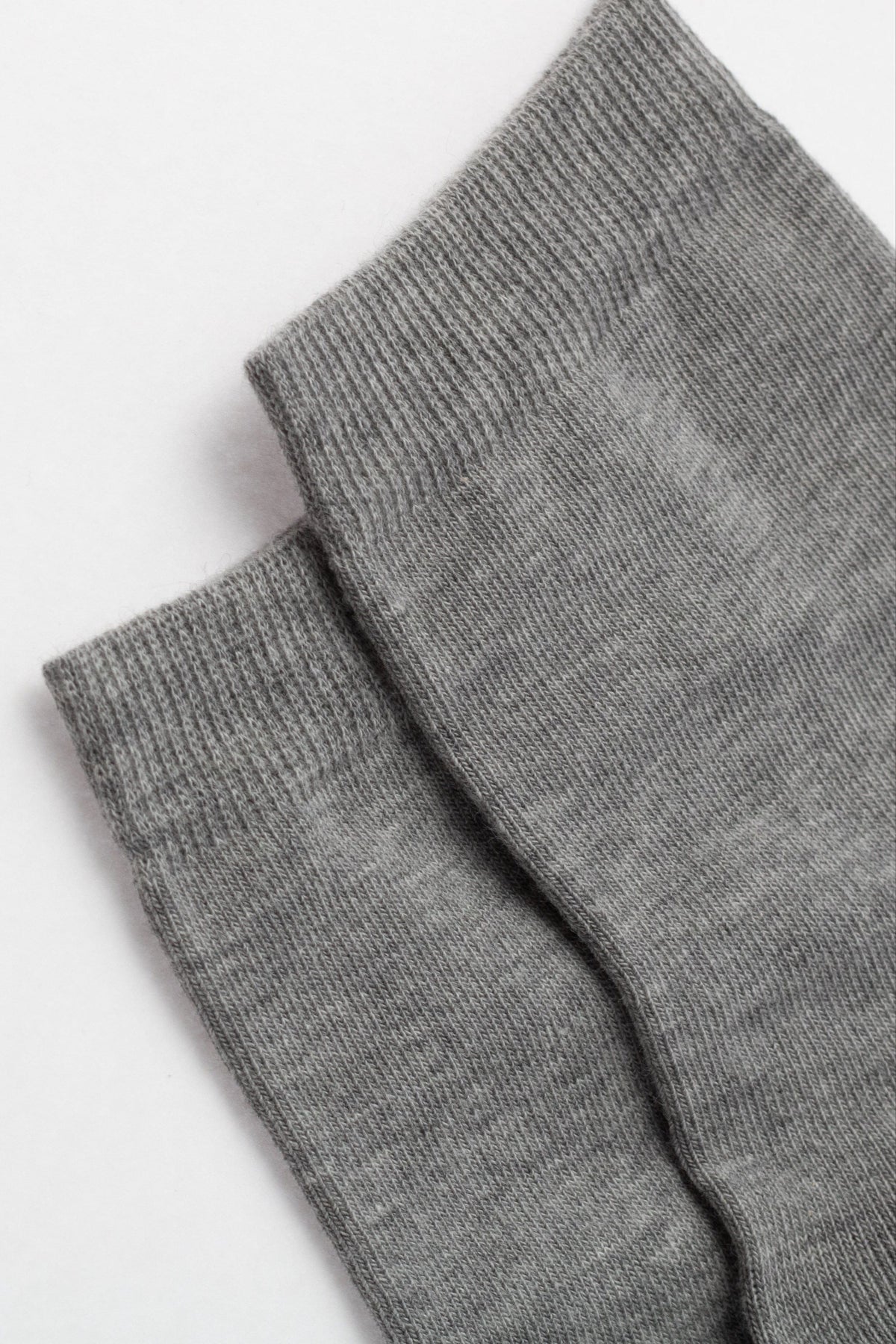 A pair of plain gray socks are folded flat, showcasing the ribbed knit cuffs and the fine, consistent texture of the fabric.