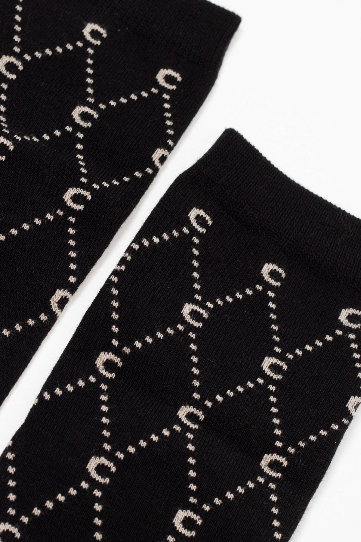 Two black socks laid side by side on a white surface feature a repeating beige geometric pattern of interlinked circles and lines.