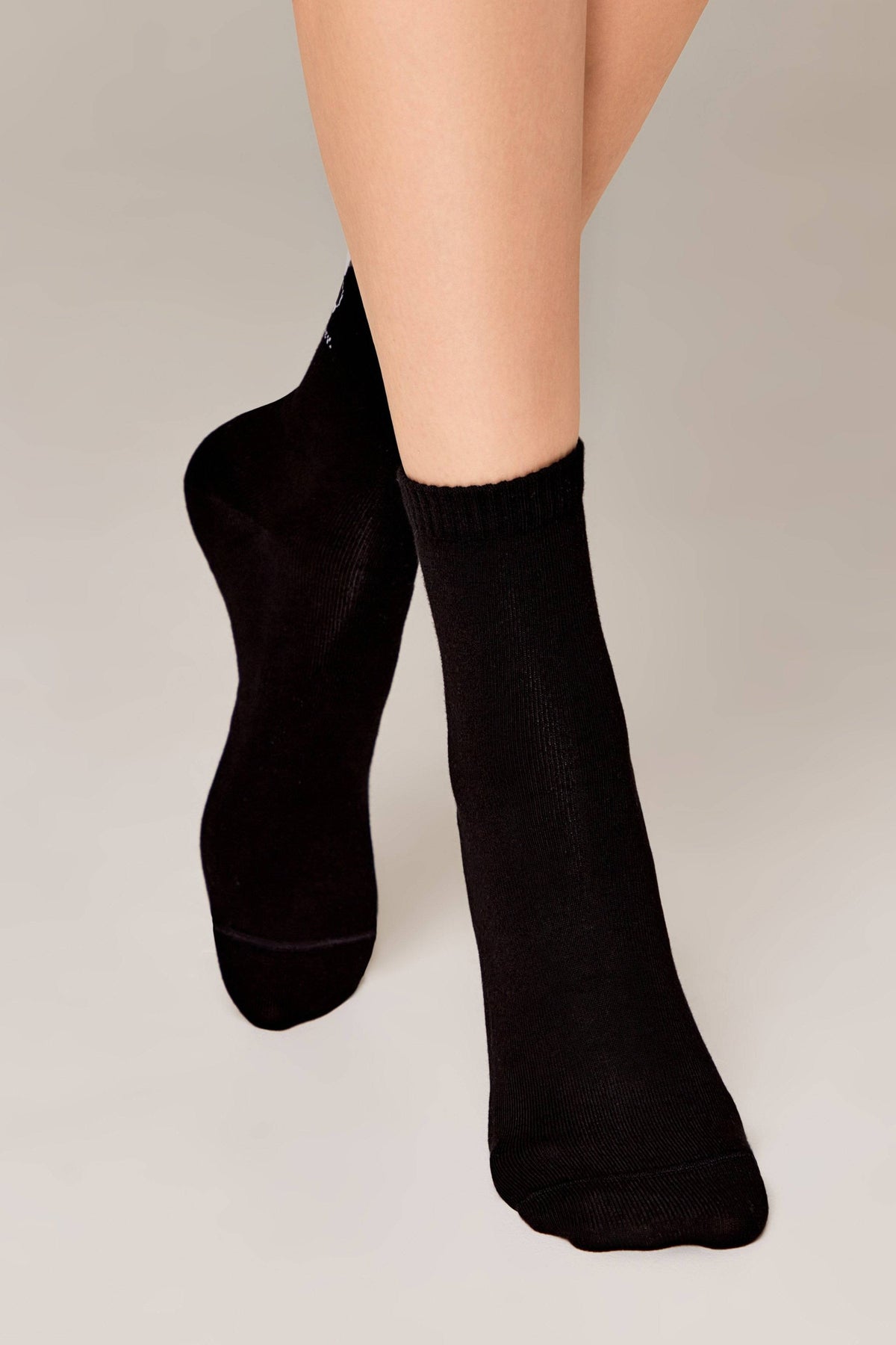 A pair of plain black crew-length socks worn on a person's feet against a neutral background.