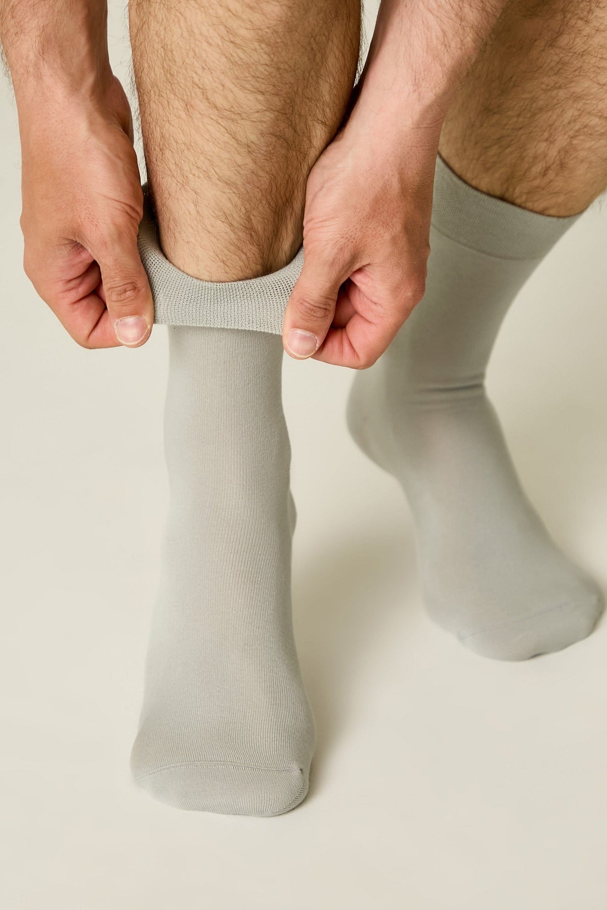 A pair of light gray crew socks worn on a person's feet, with hands shown pulling up the cuff of one sock.