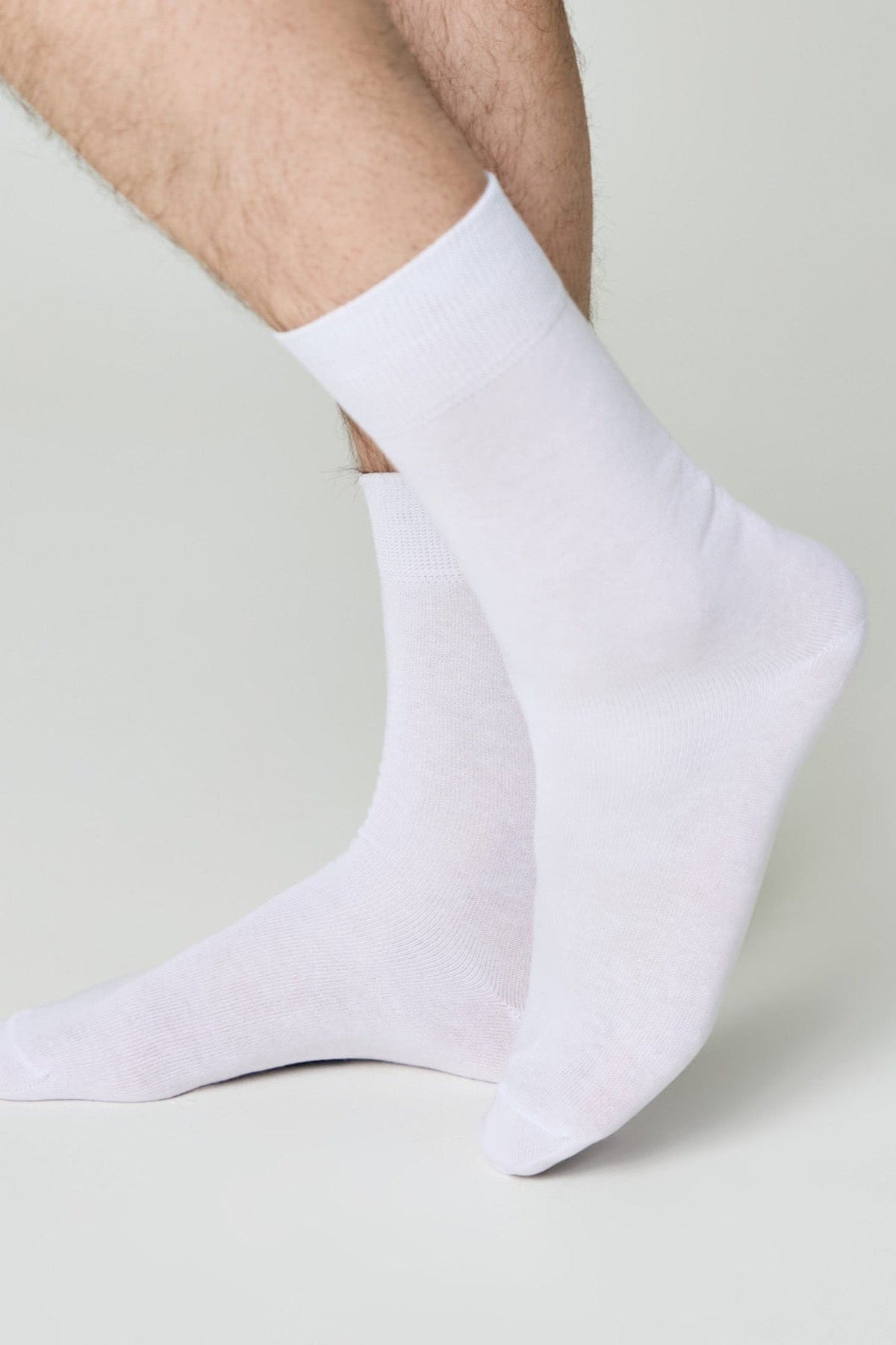 A pair of plain white crew socks worn on a person's feet against a plain light gray background.