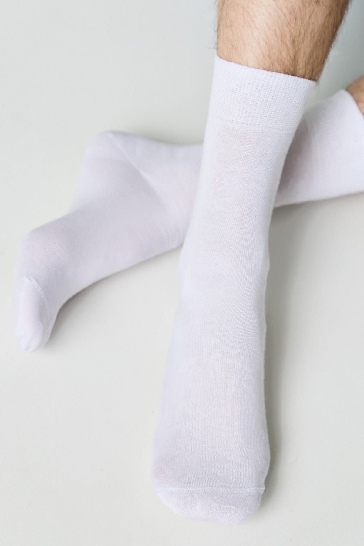 A pair of plain white crew socks worn on a person's feet against a neutral background.