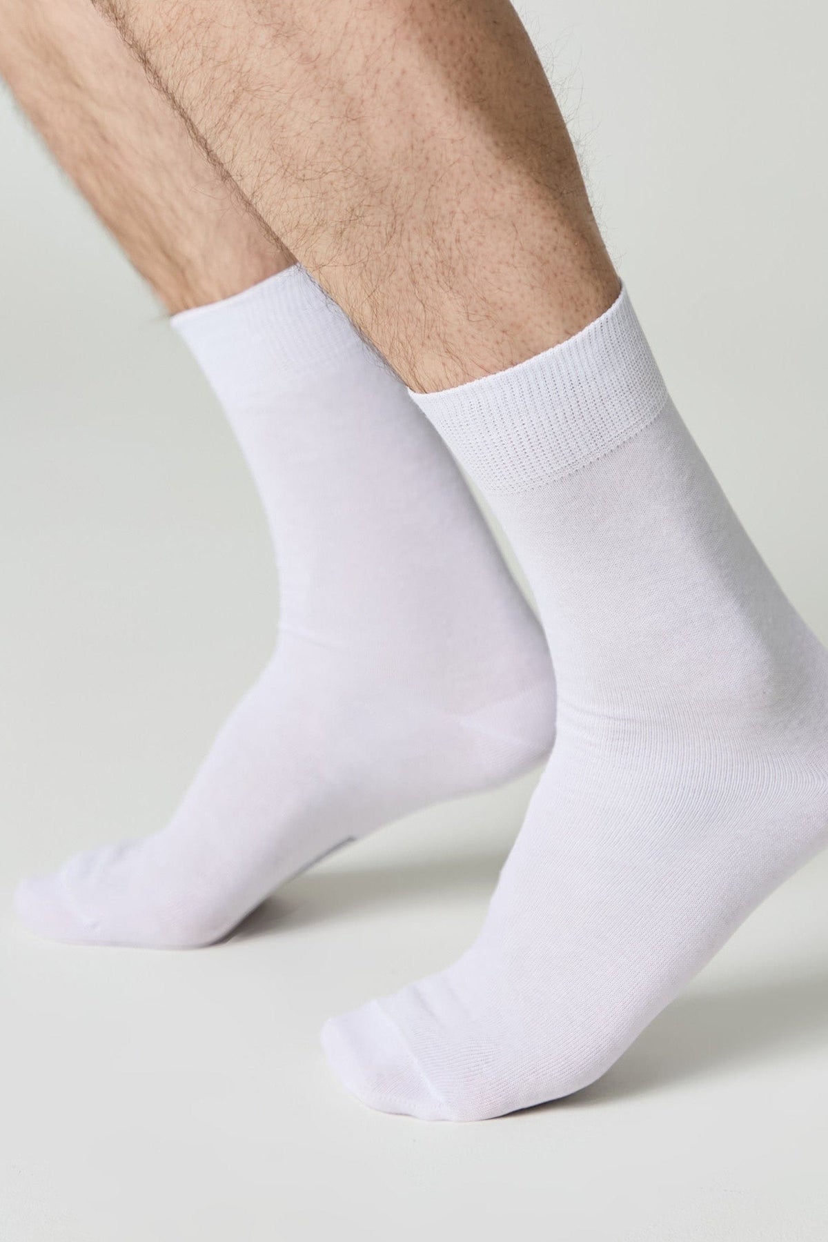 A pair of plain white crew socks worn on a person's feet against a neutral background.