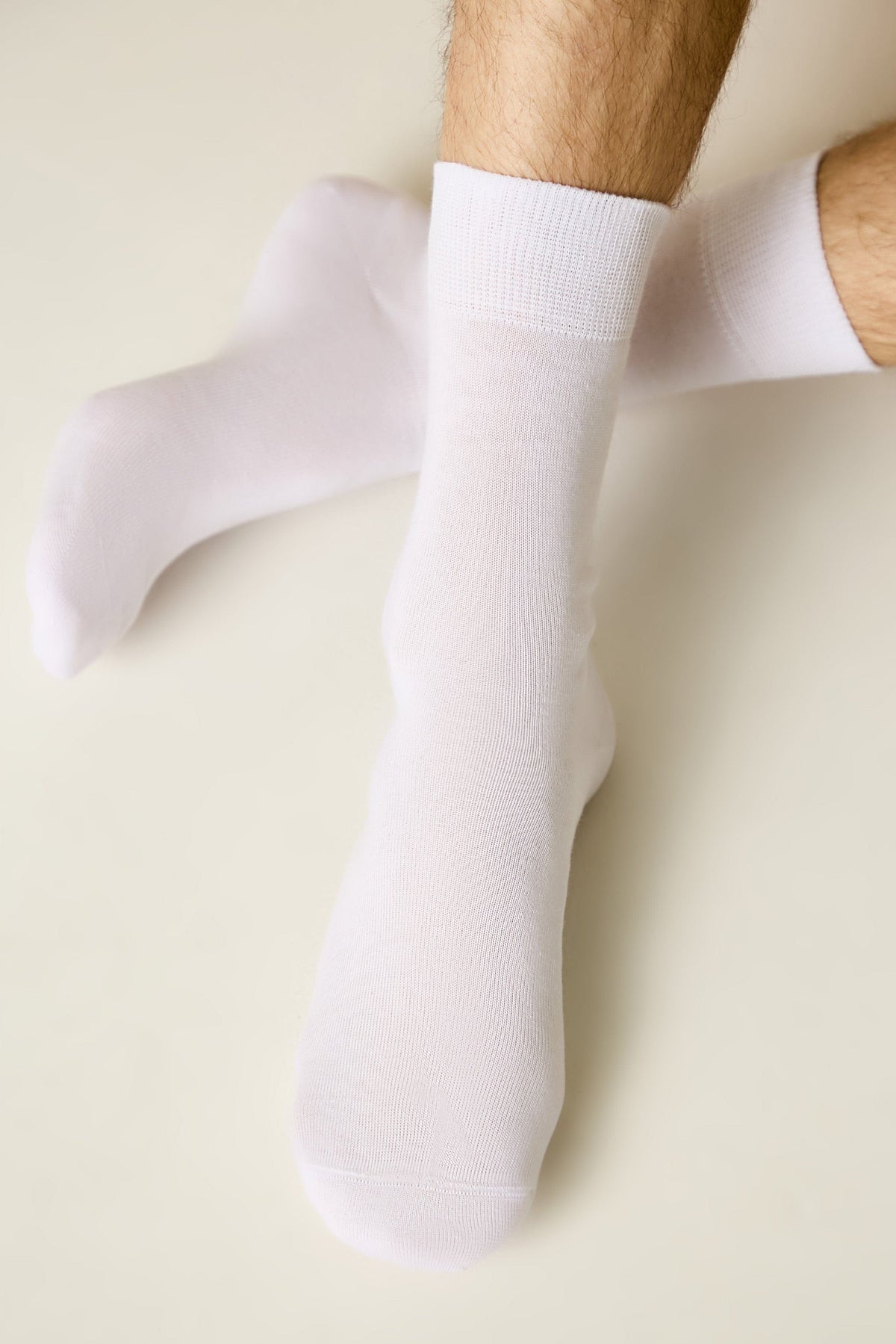 A pair of plain white crew socks worn on a person's feet against a light cream background.
