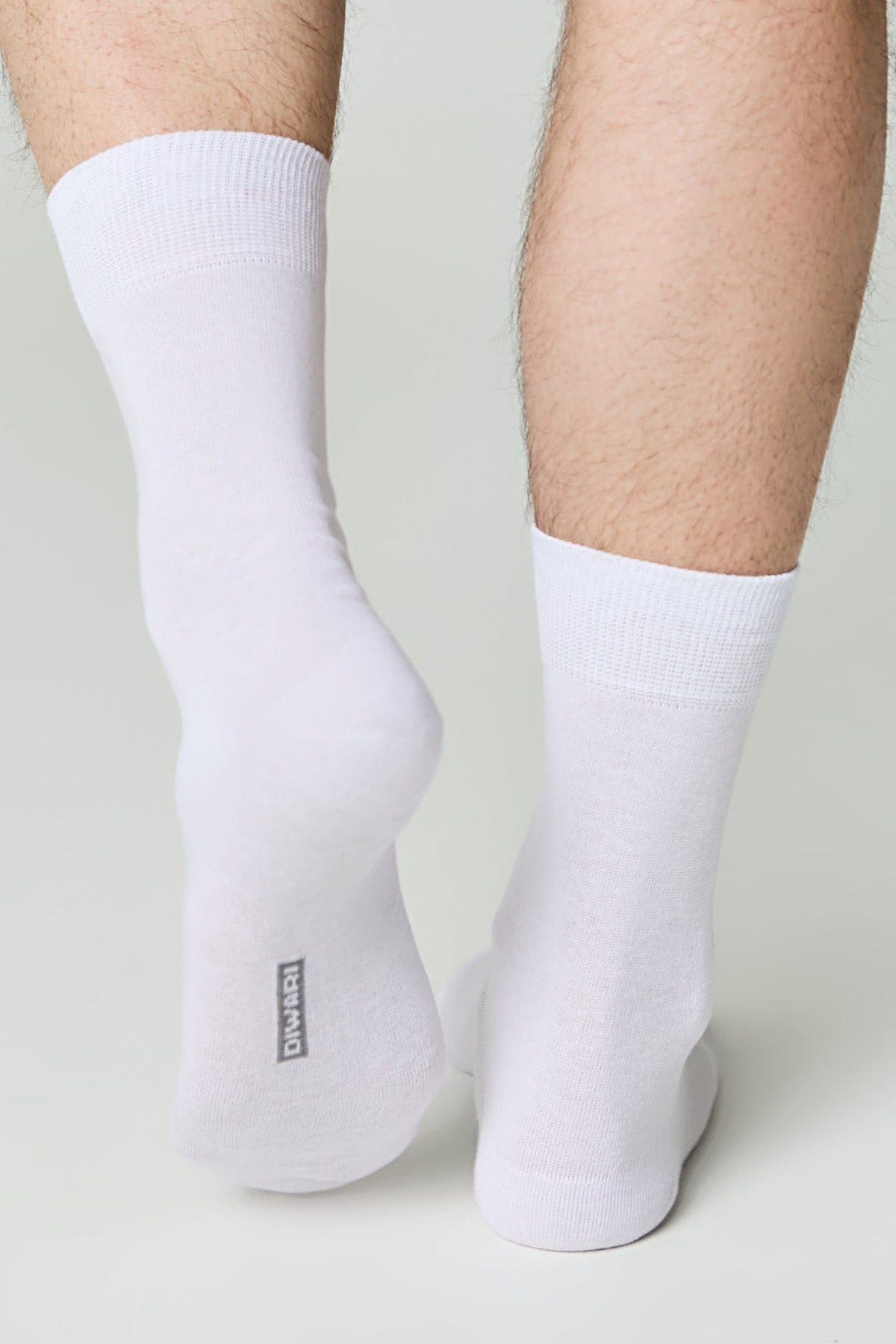A pair of plain white mid-calf socks worn on a person's feet against a light grey background.