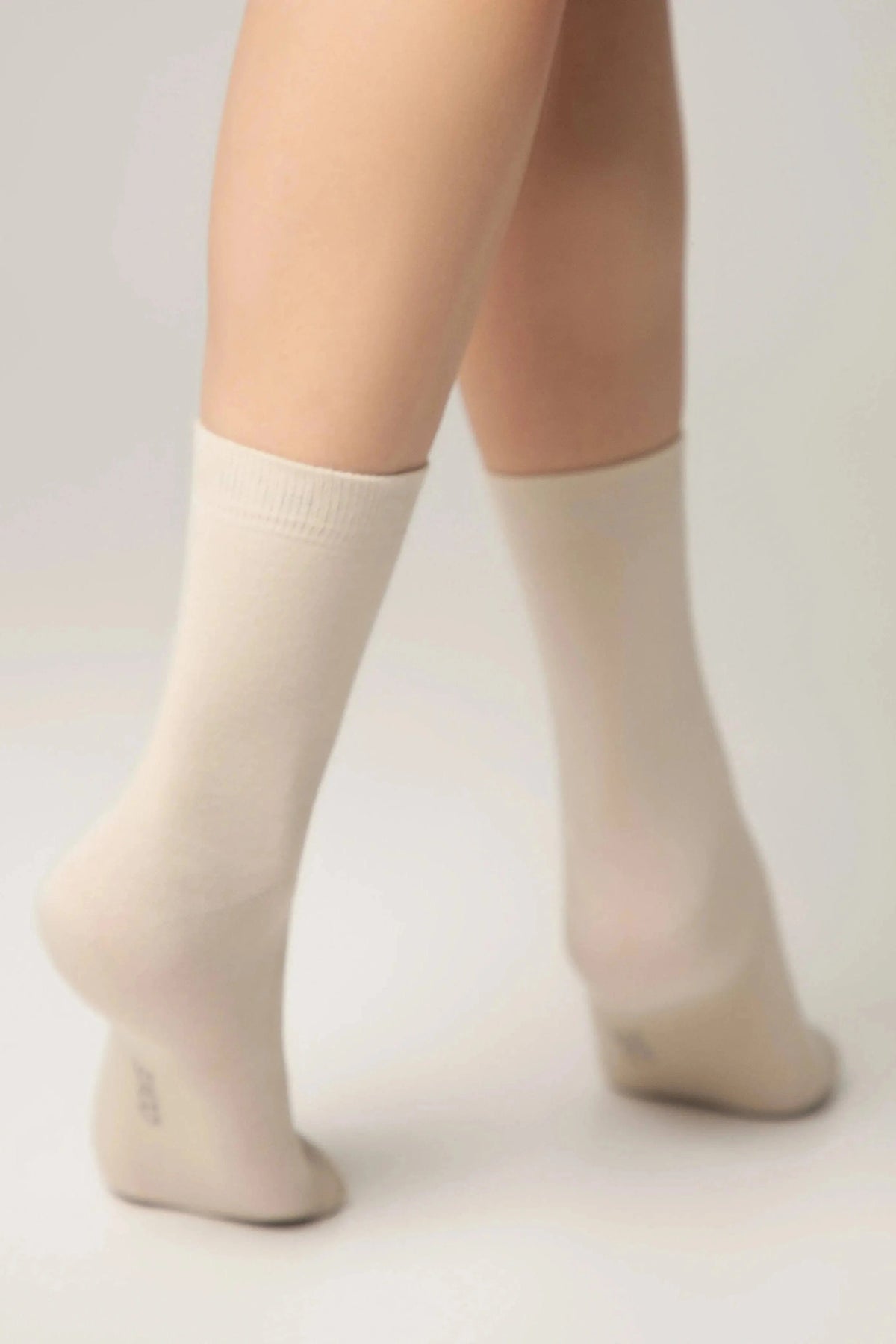 A pair of beige crew socks worn on a person standing on their tiptoes against a neutral background.