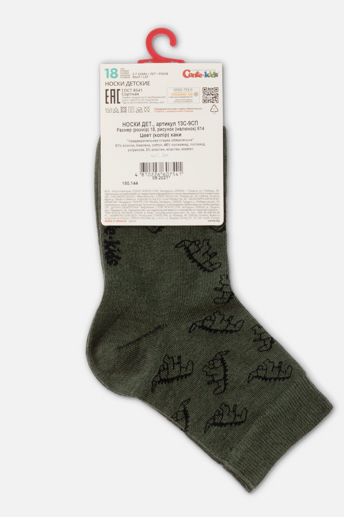 Olive green ankle socks featuring a black dinosaur pattern with a white cardboard product information tag attached to the top.