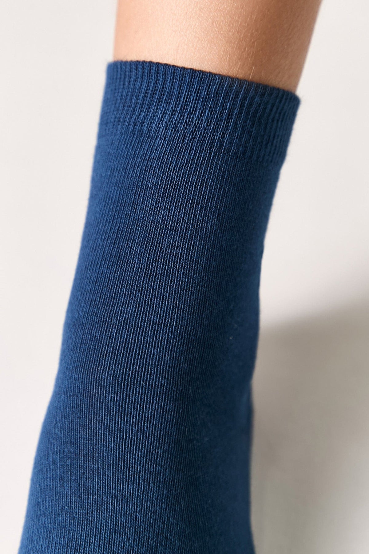 A close-up of a blue sock worn on a person's ankle against a plain, light background.