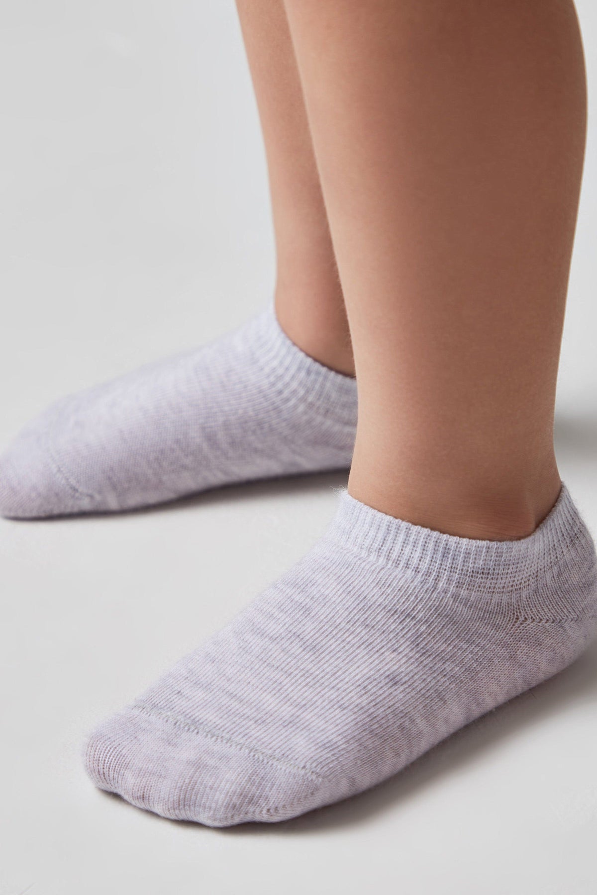 A pair of low-cut, light grey textured socks worn on a person's feet against a plain white background.