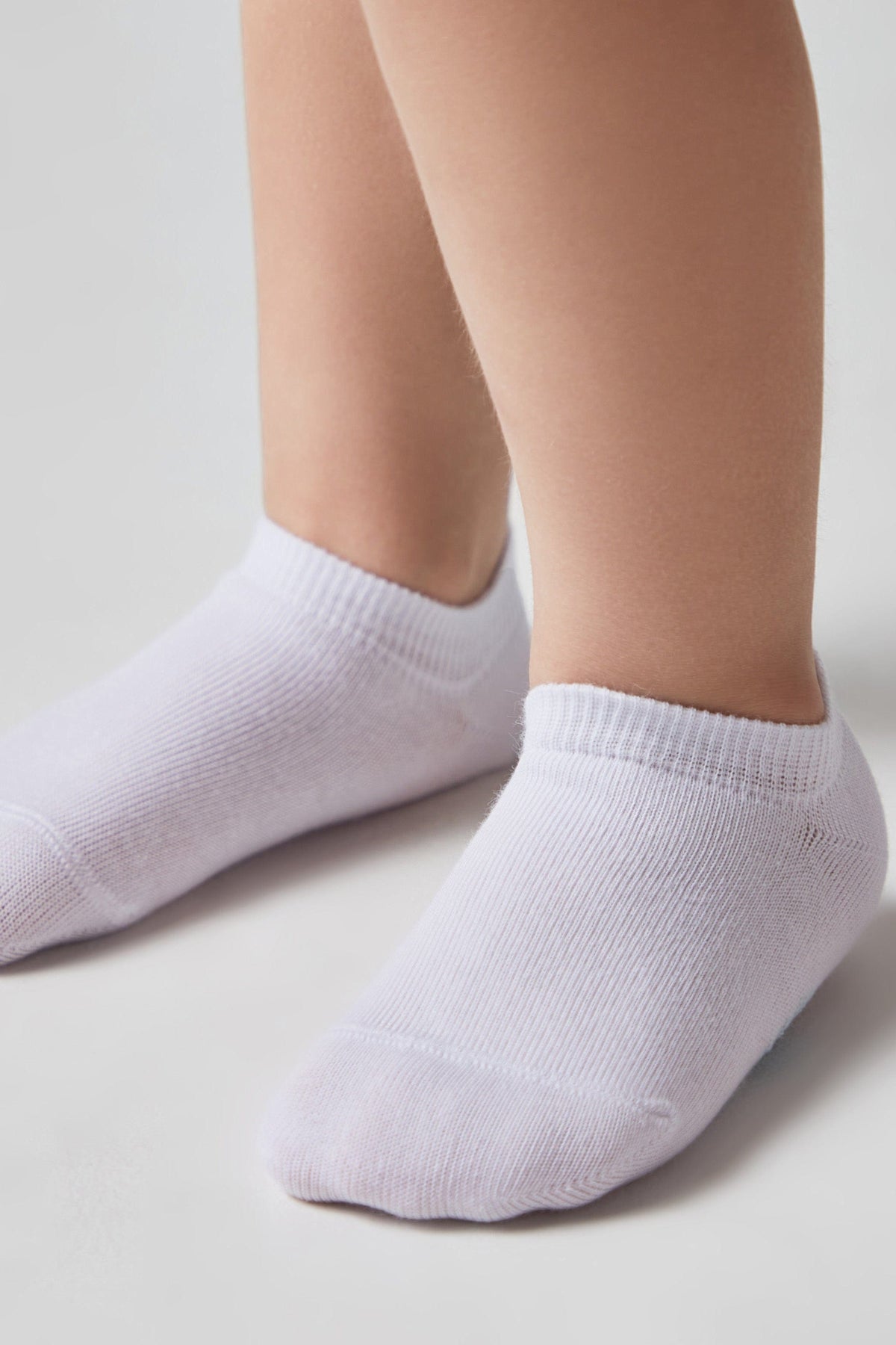 A pair of white low-cut ankle socks are worn on a person's feet against a plain light background.
