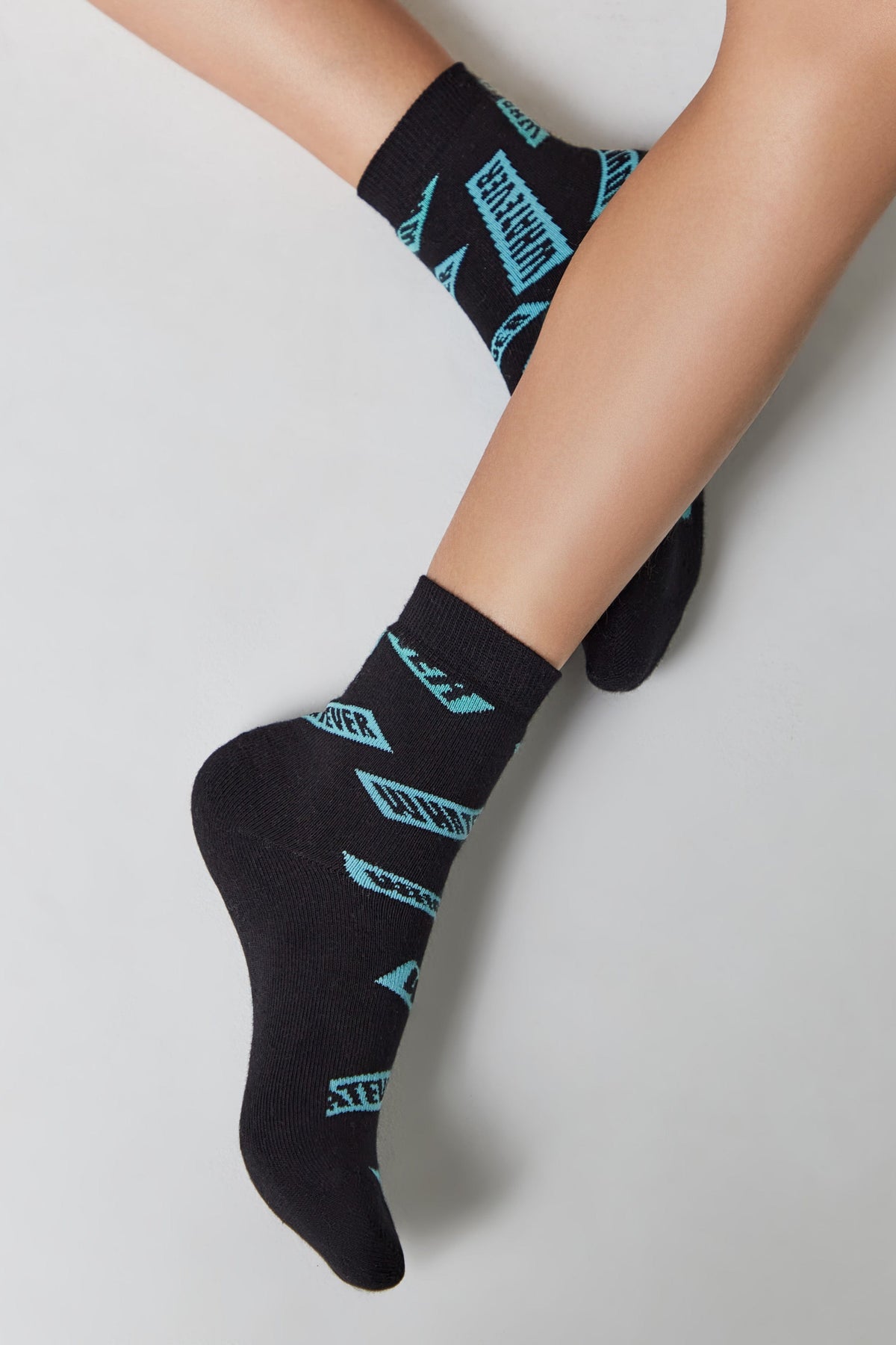 Black ankle socks featuring a repeated light blue text pattern displayed on a pair of legs against a plain light gray background.