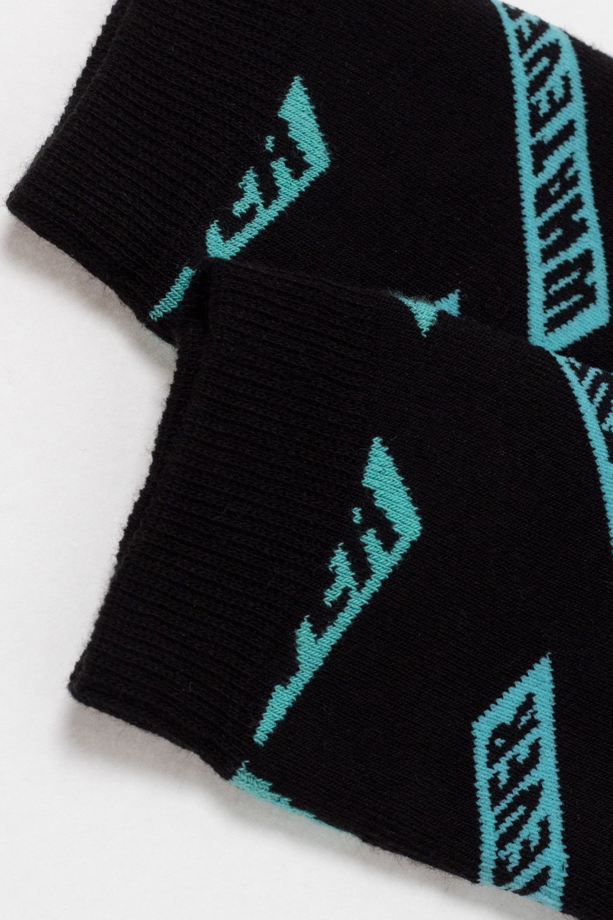 A pair of black crew socks featuring a repeating teal geometric graphic pattern on a white background.