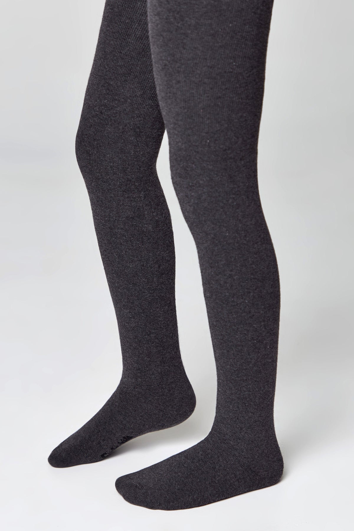 A pair of dark charcoal grey tights with ribbed texture worn on a person's legs against a plain white background.