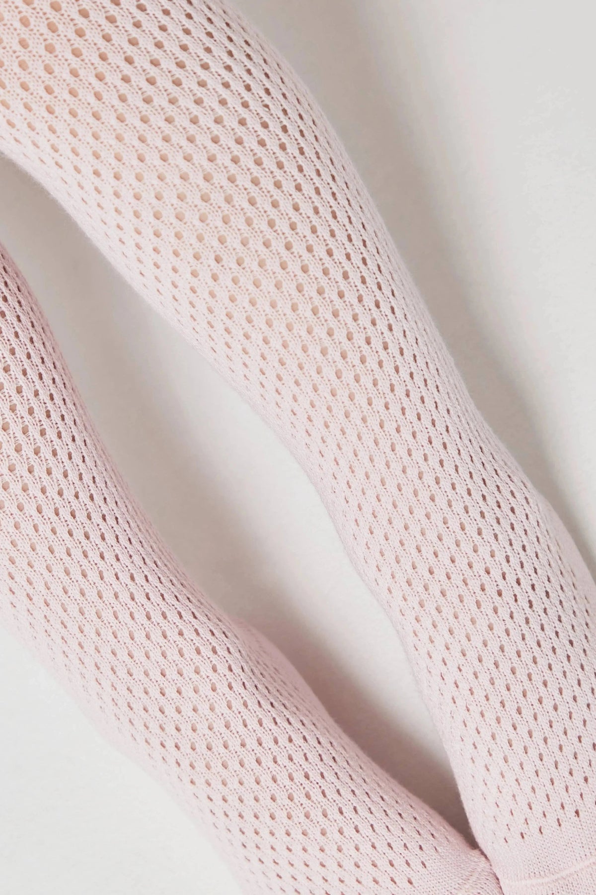 A close-up view of two legs wearing pale pink, fine-knit, open-weave tights against a plain white background.