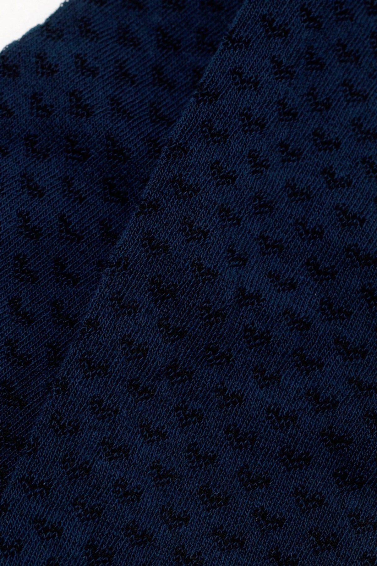 A close-up of dark navy blue fabric featuring a textured geometric pattern of small, repeating shapes.