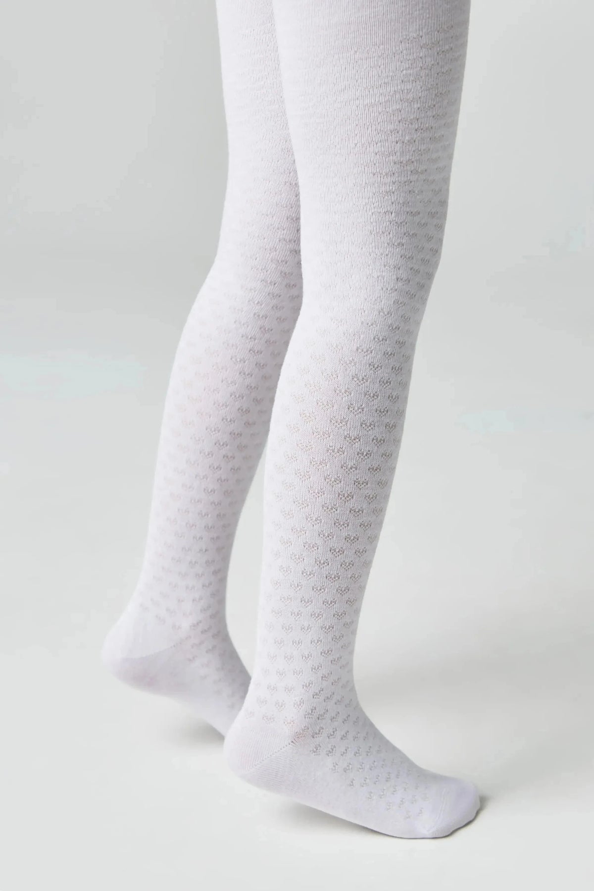 A pair of white tights for a child feature a repeating subtle heart pattern throughout against a plain light gray background.