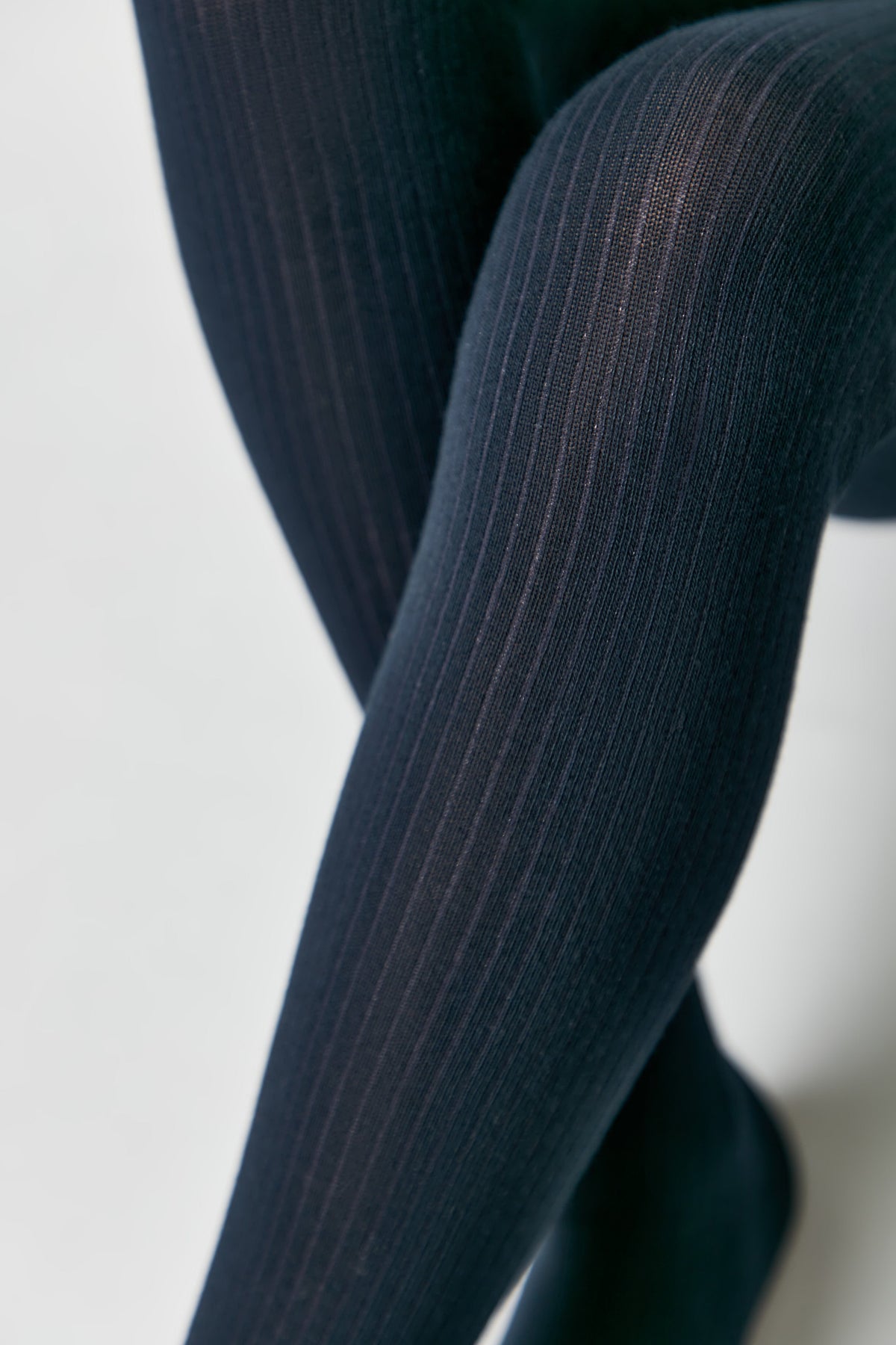 A close-up view of legs wearing opaque, dark navy blue ribbed tights against a plain white background.