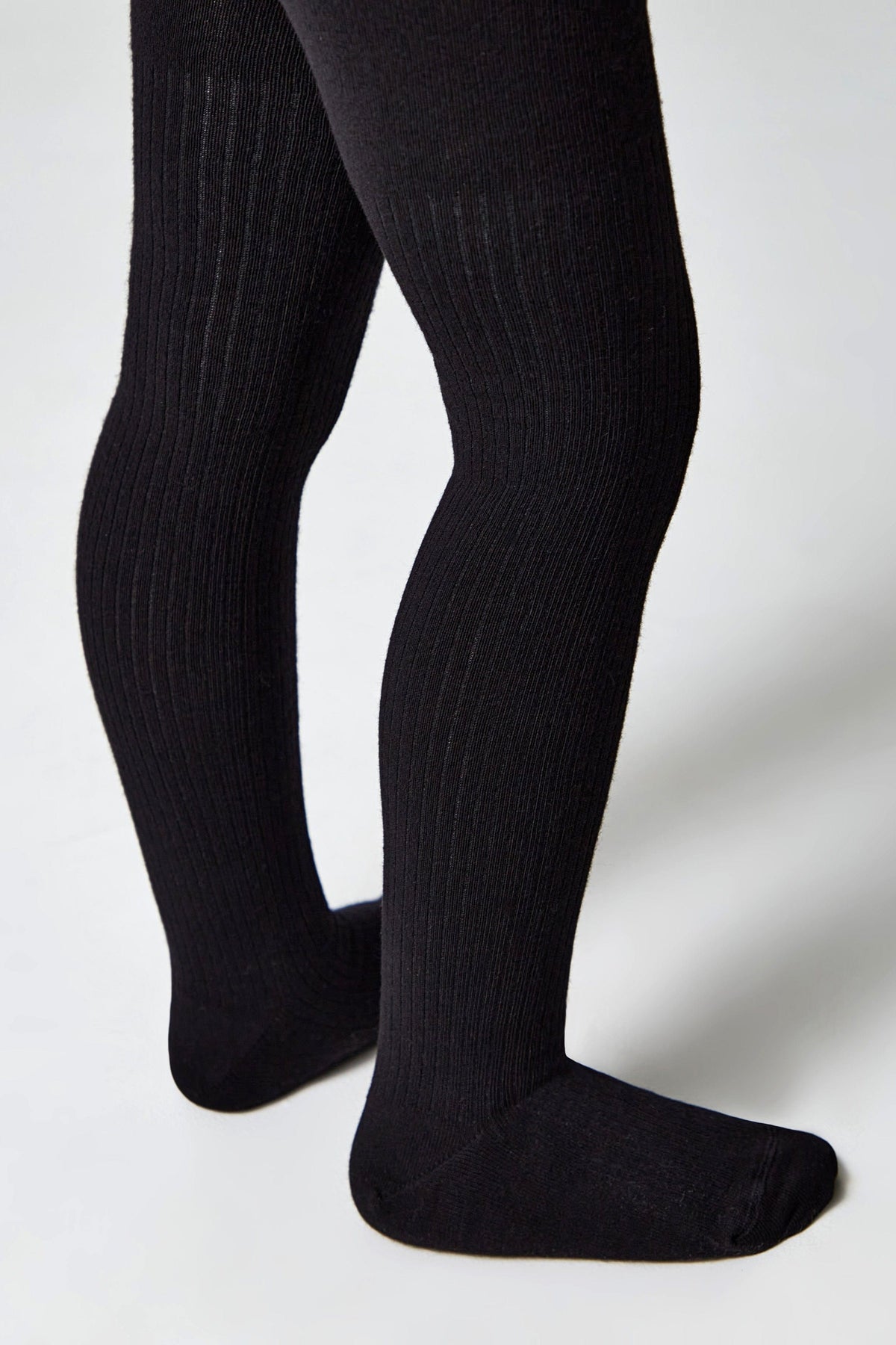 A pair of black ribbed tights worn on a child's legs against a plain white background.