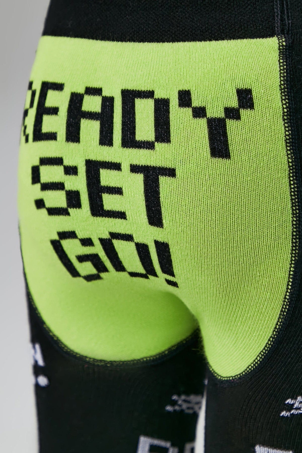 A close-up of neon green leggings featuring the pixelated black text READY SET GO! on the seat, with black fabric sections visible on the sides and thighs.