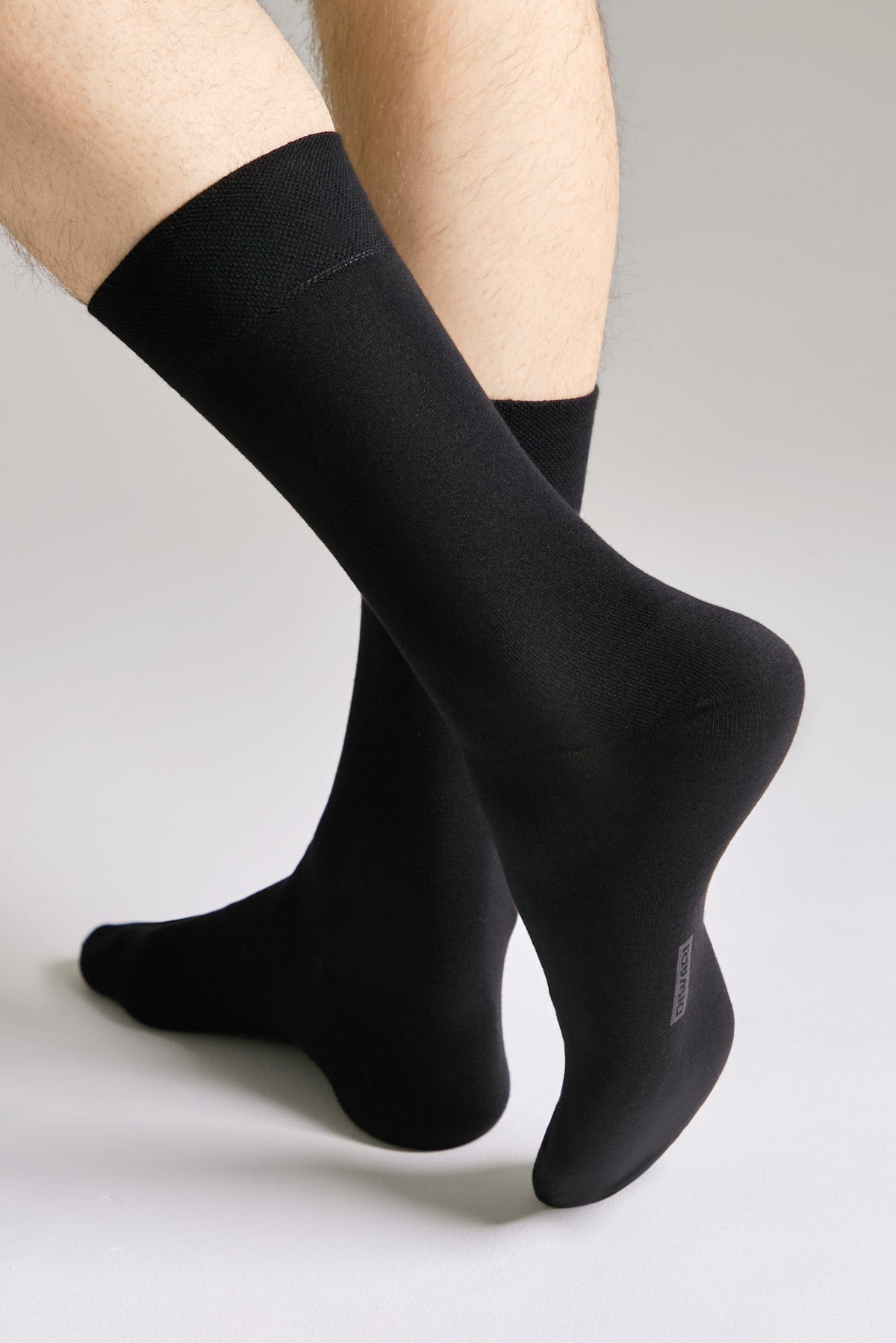 A pair of black crew-length socks worn on a person's legs against a light grey background.