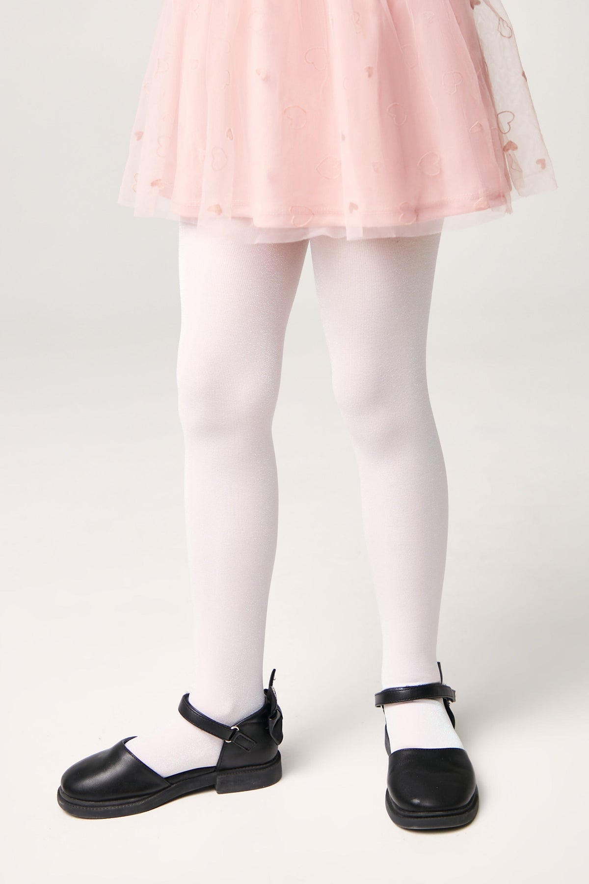 A pair of opaque white tights worn with a light pink heart-patterned tulle skirt and black mary jane shoes.