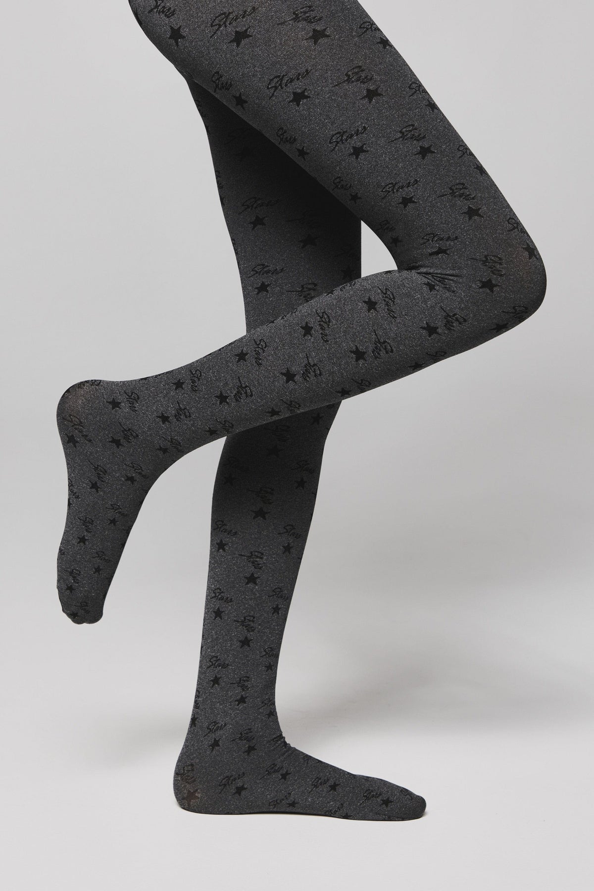 Gray tights with an all-over black star and cursive text pattern worn on the legs of a person against a neutral background.