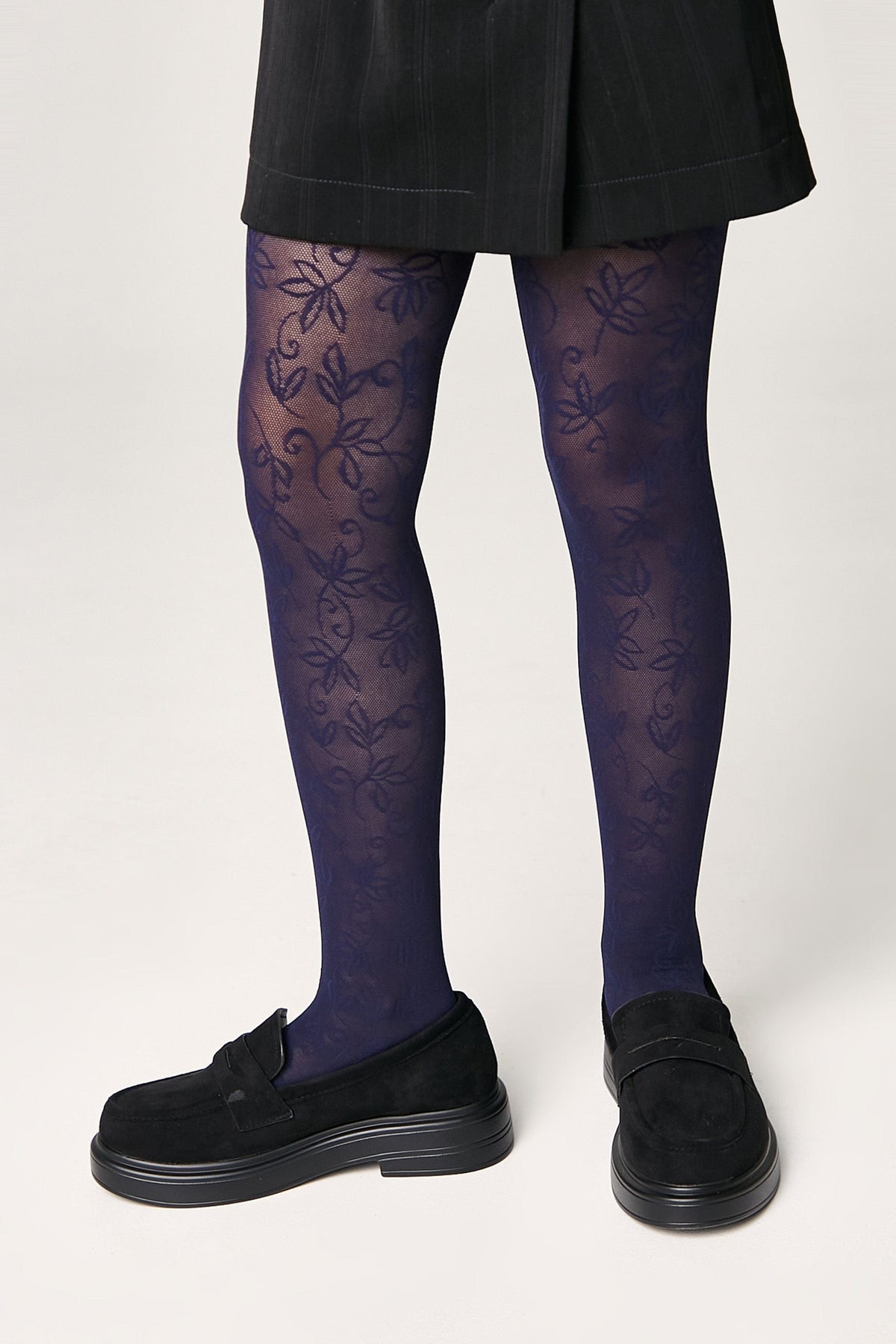 Blue tights featuring a delicate floral pattern worn with a black mini skirt and black platform loafers.