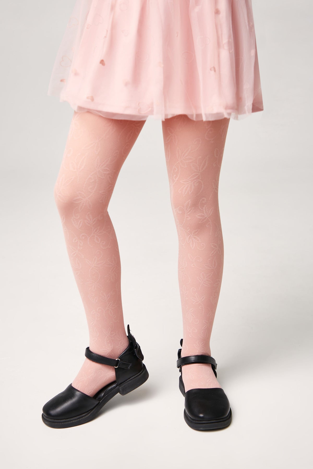A child wears light pink floral patterned tights paired with black buckled mary jane shoes and a matching pink skirt.