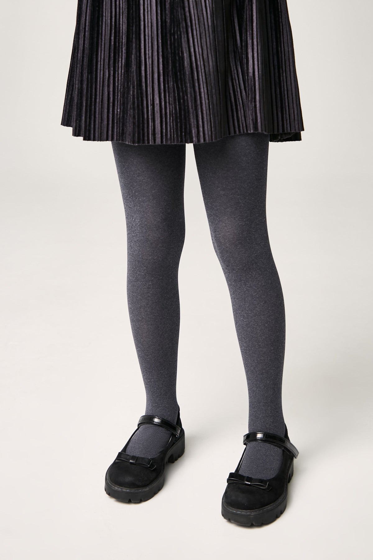 A pair of opaque charcoal grey tights paired with a black pleated skirt and black Mary Jane shoes with low platform soles.