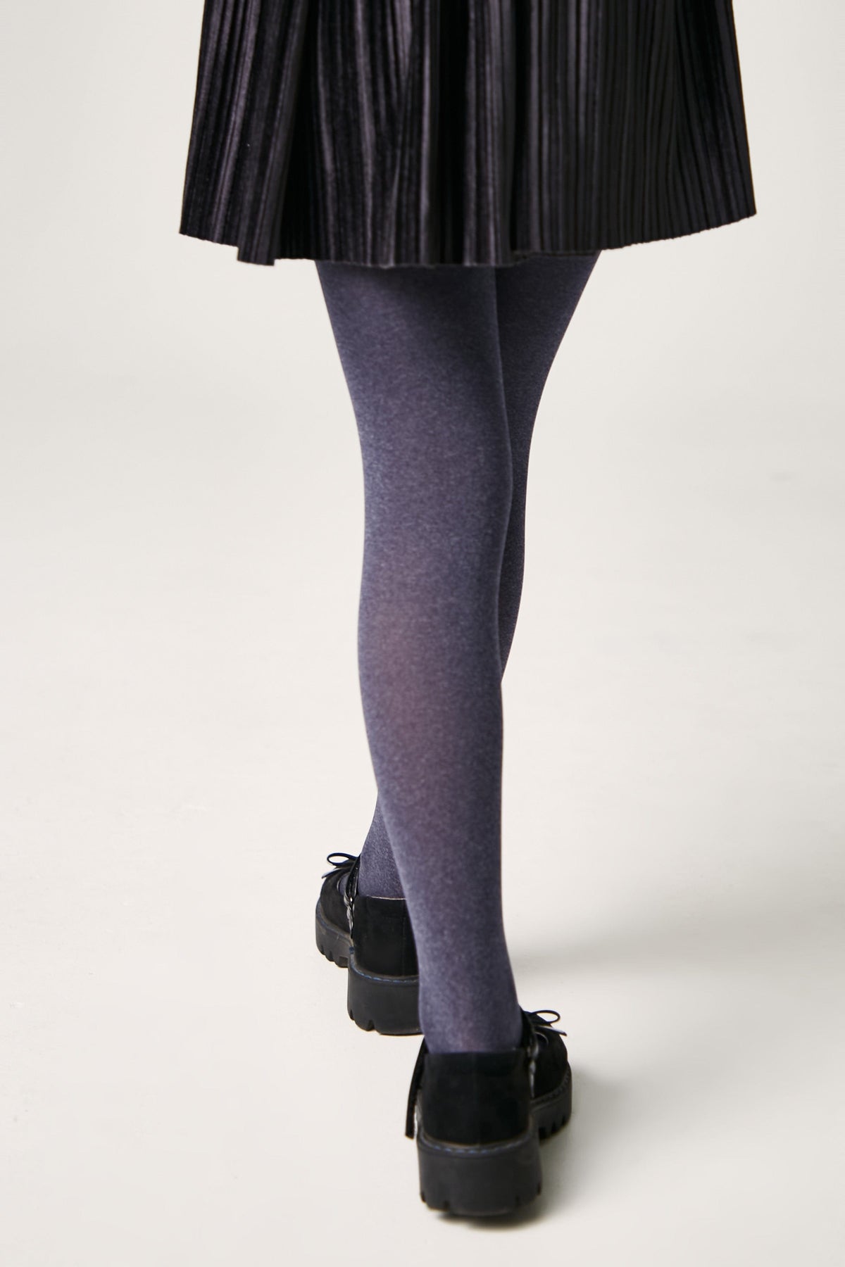 A person wearing dark grey tights and black platform shoes with a black pleated skirt.