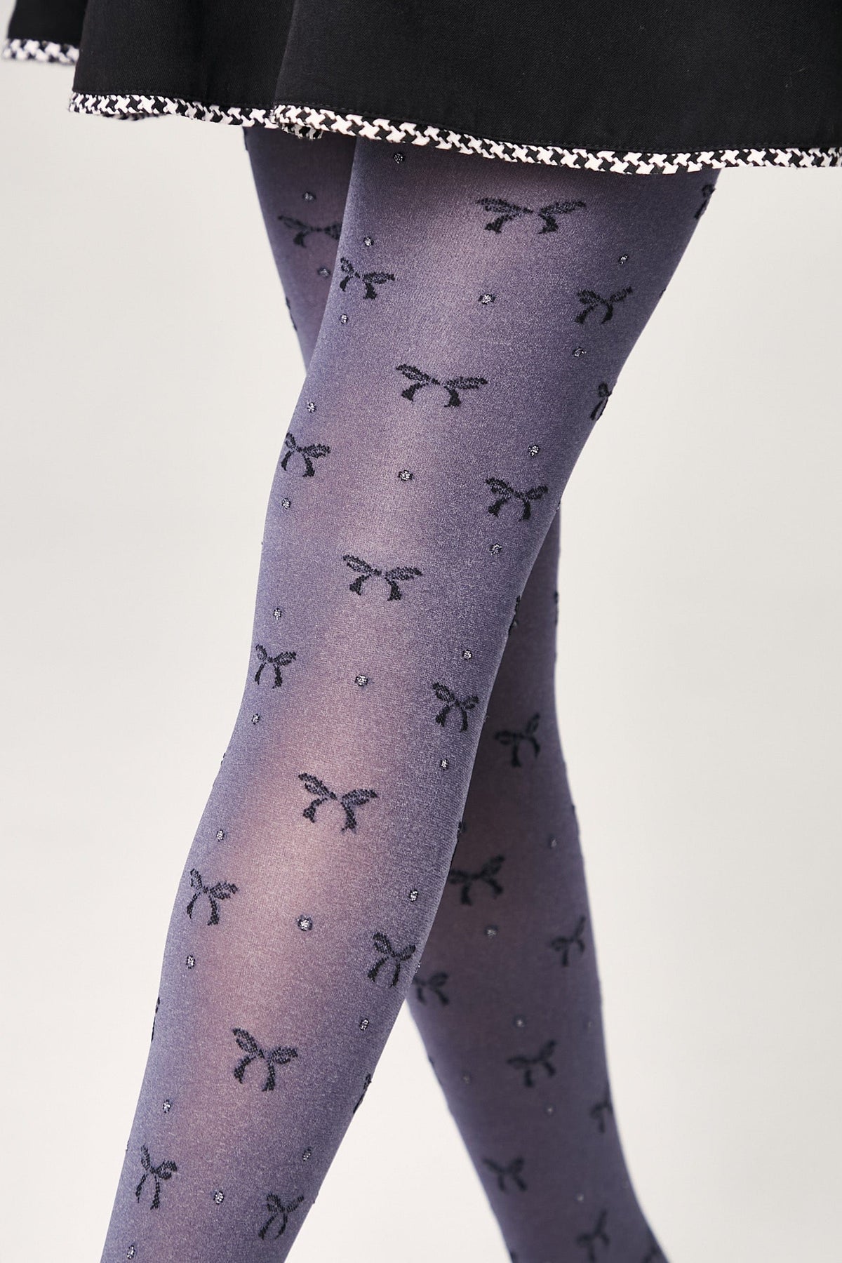 Blue-grey patterned tights featuring a repeating motif of small dark bows and tiny shimmering dots on a person wearing a black skirt.