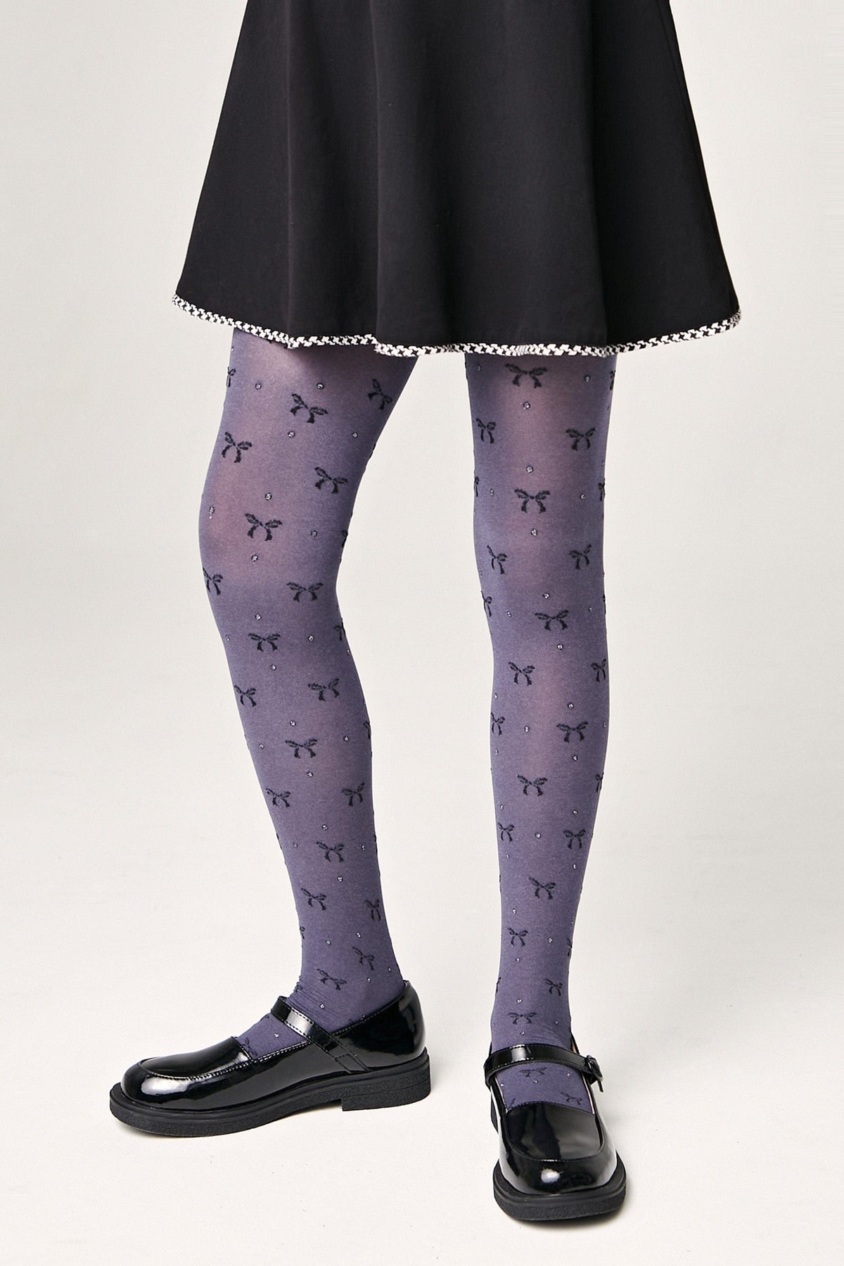 Grayish-purple tights patterned with small black bows and tiny rhinestones worn with a black skater skirt and black patent leather mary jane shoes.