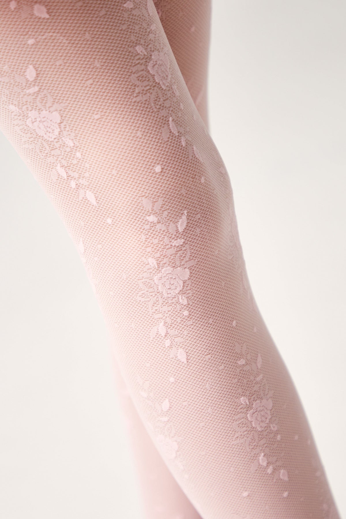A close-up view of light pink floral patterned tights worn on legs against a plain white background.